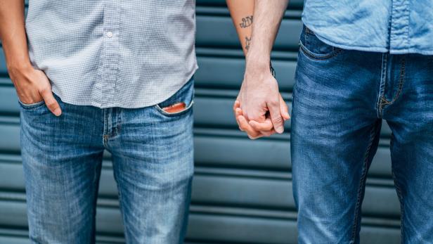 Zwei Männer halten Händchen vor einem Rolltor.