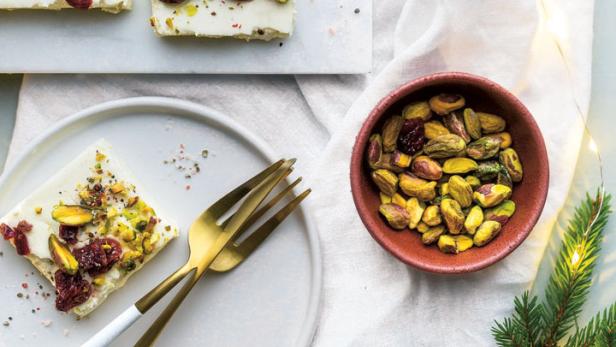 Quadrate aus weißem Fudge, garniert mit Pistazien und Cranberries, auf einem Tisch präsentiert.