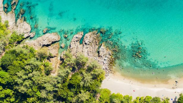 Luftaufnahme eines Strandes mit türkisfarbenem Wasser und üppiger Vegetation.