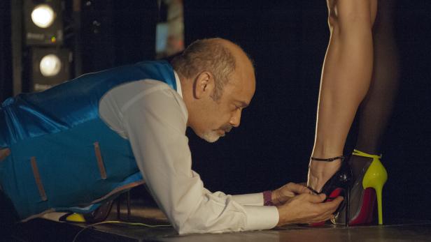 Ein Mann kniet und schliesst einer Frau den Riemen ihres High Heels mit gelbem Absatz.