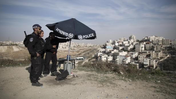 Drei Polizisten stehen unter einem Sonnenschirm mit der Aufschrift „Police“ und blicken auf eine Stadt.