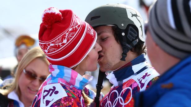 Ein Paar in Winterkleidung küsst sich vor einem verschwommenen Hintergrund.
