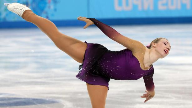 Eine Eiskunstläuferin in einem lila Kleid führt eine Pirouette auf dem Eis aus.