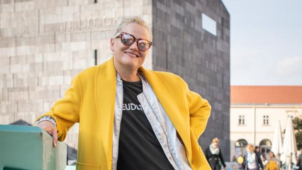 Eine Frau mit gelbem Mantel und Zebrahose posiert vor dem mumok in Wien.