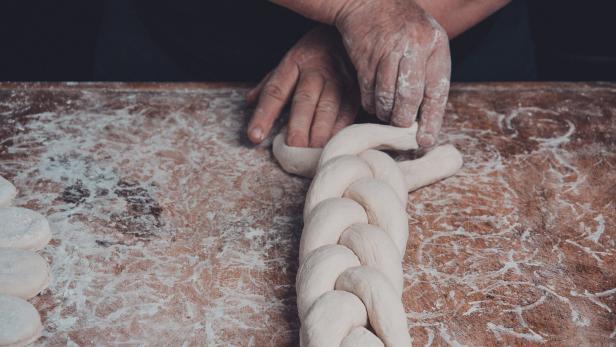 Hände flechten einen Teigstrang auf einer bemehlten Arbeitsfläche.