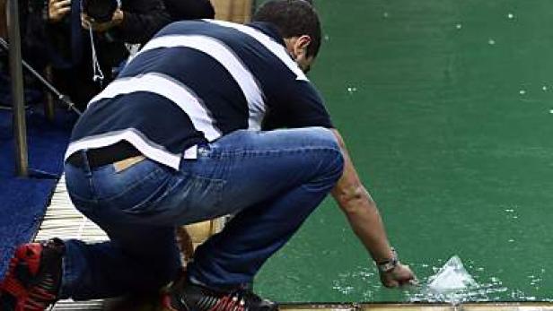 Ein Mann kniet am Beckenrand und berührt das grüne Wasser.