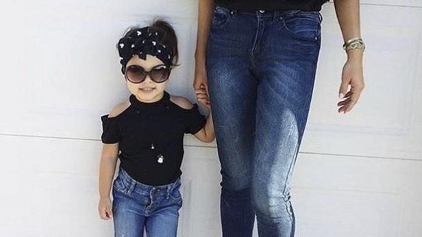 Ein kleines Mädchen mit Sonnenbrille und Stirnband hält die Hand einer erwachsenen Person.