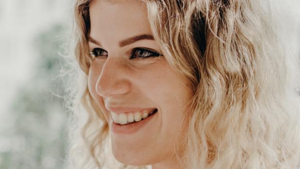 Eine lächelnde Frau mit blonden Locken hält eine Tasse Kaffee.