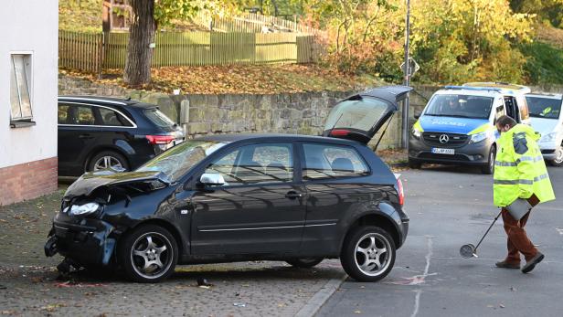 Ein Polizist untersucht hinter einem schwarzen VW Polo vor einer Kindertagesstätte im Ortsteil Gertenbach den Unfallhergang.