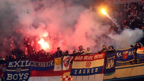 Fußballfans zünden während eines Spiels Rauchbomben und halten Banner hoch.