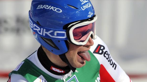 Ein Skirennläufer mit blauem Helm und Skibrille streckt die Zunge heraus.