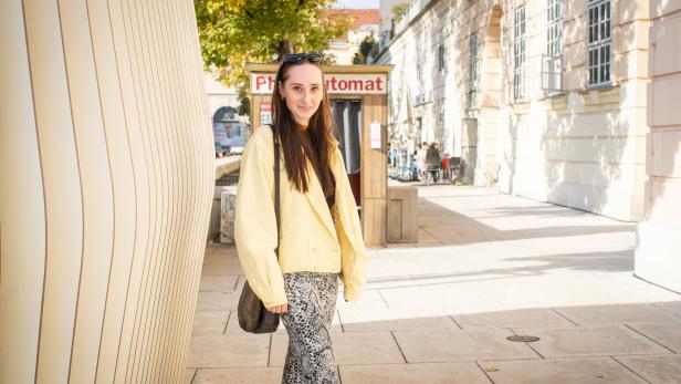Eine junge Frau posiert vor einem Fotoautomaten in einer städtischen Umgebung.