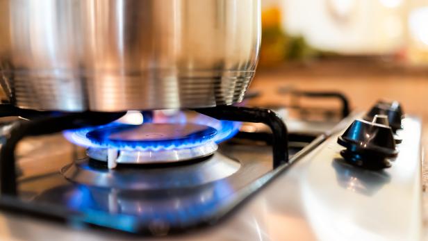Brennenede Flamme eines Gasherdes mit Topf darüber.