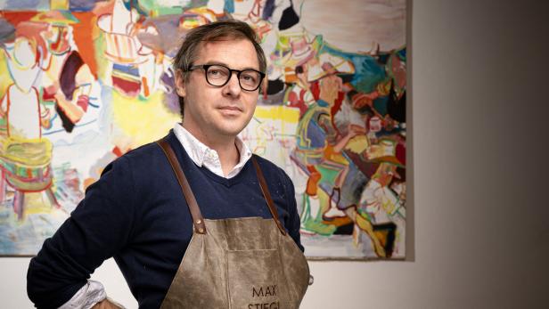 Max Stiegl, ein Künstler, steht vor einem seiner farbenfrohen Gemälde.