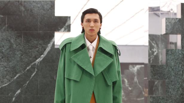 Ein Mann trägt einen grünen Trenchcoat und einen braunen Anzug mit einer braunen Aktentasche.