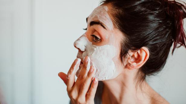 Eine Frau trägt eine weiße Gesichtsmaske auf ihr Gesicht auf.