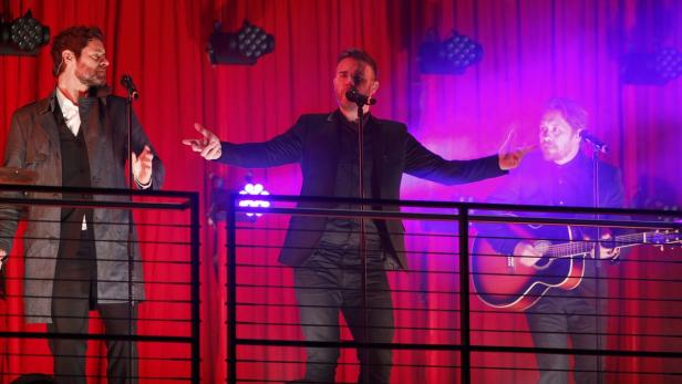 Take That tritt auf einer Bühne mit rotem Vorhang auf.