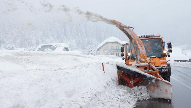 Ein orangefarbener Schneepflug räumt eine Straße von Schnee frei.