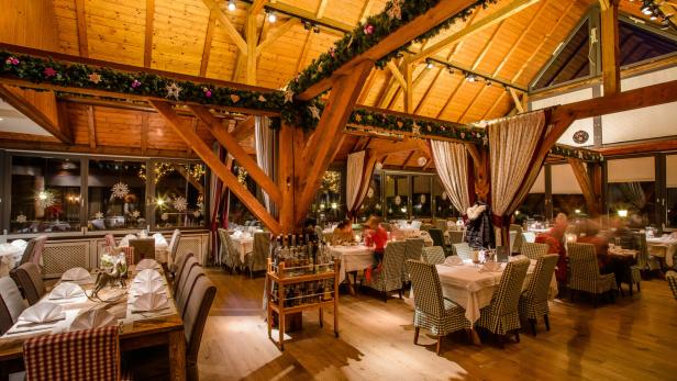 Ein festlich geschmücktes Restaurant mit Holzbalkendecke und gedeckten Tischen.