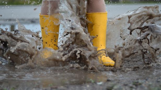 Gelbe Gummistiefel springen in eine schlammige Pfütze.