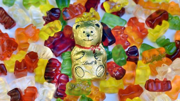 Ein goldener Lindt-Schokoladenbär liegt inmitten von bunten Gummibärchen.