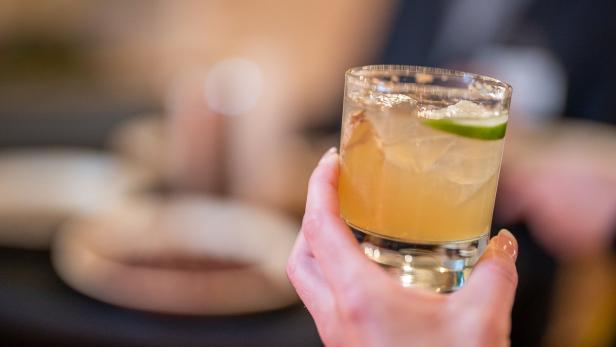 Eine Hand hält ein Glas mit einem Cocktail und einer Limettenscheibe.