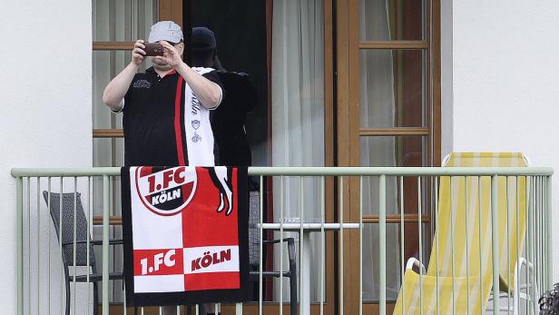 Ein Mann fotografiert von einem Balkon mit einem 1. FC Köln-Handtuch.