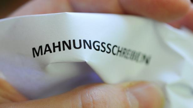 Eine Hand hält ein Blatt Papier mit der Aufschrift „MAHNUNGSSCHREIBEN“.