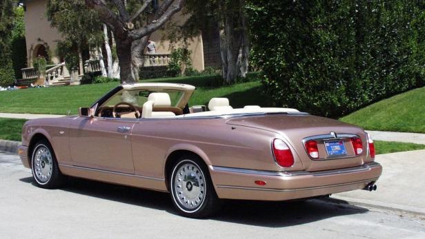 Ein rosafarbenes Bentley Cabriolet parkt vor einem Haus mit gepflegtem Rasen.