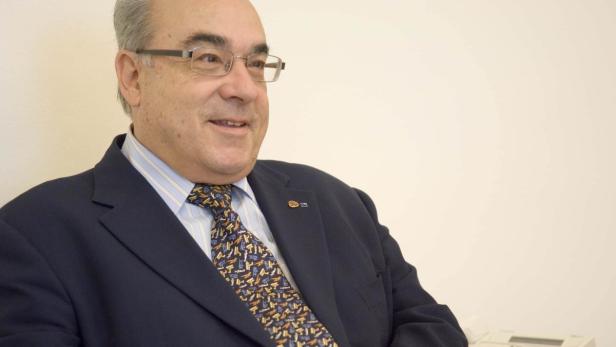 Ein Mann mit Brille, Anzug und Krawatte lächelt.