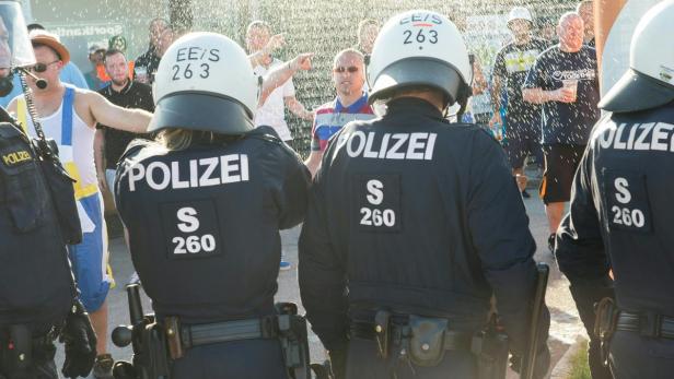 Polizisten stehen vor einer Menschenmenge, aus der Wasser auf sie gespritzt wird.