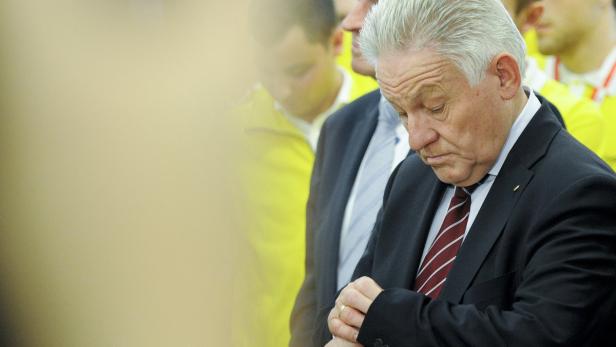 Ein älterer Mann im Anzug blickt auf seine Armbanduhr.