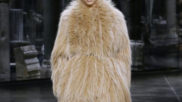 Ein Model präsentiert einen langen, beigen Pelzmantel auf einem Laufsteg.