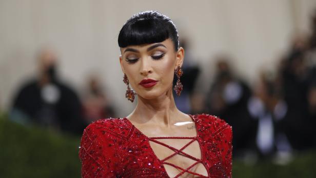 Megan Fox in einem roten, tief ausgeschnittenen Kleid mit passenden Ohrringen.