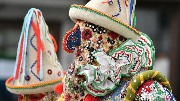 Zwei Personen tragen aufwendige, farbenfrohe Masken und Hüte, vermutlich für eine traditionelle Feierlichkeit.