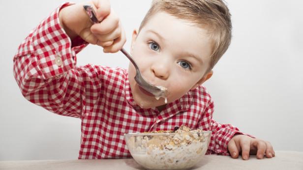 Ein Junge im karierten Hemd isst Müsli mit einem Löffel.