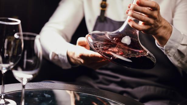 Ein Kellner dekantiert Rotwein in einem eleganten Dekanter.