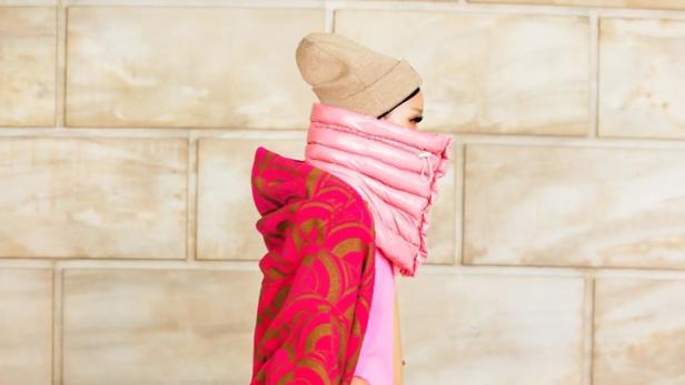 Ein Model präsentiert ein auffälliges Outfit in Pink und Gold mit passender Mütze.