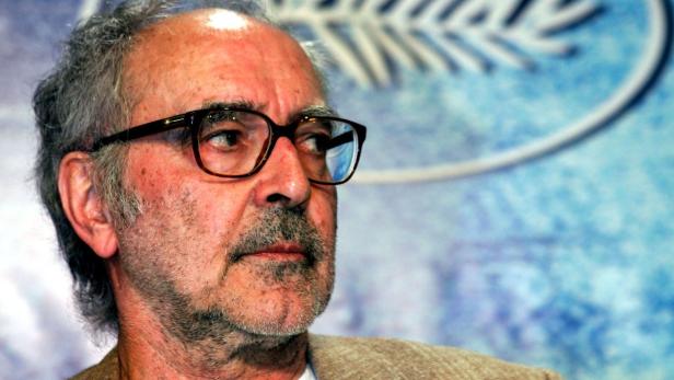 Nahaufnahme von Jean-Luc Godard mit Brille vor einem blauen Hintergrund.