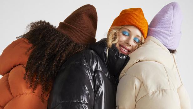 Drei Frauen in bunten Daunenjacken und Mützen stehen eng nebeneinander.