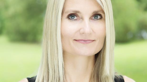 Porträt einer Frau mit blonden, schulterlangen Haaren und einem schwarzen Oberteil vor grünem Hintergrund.