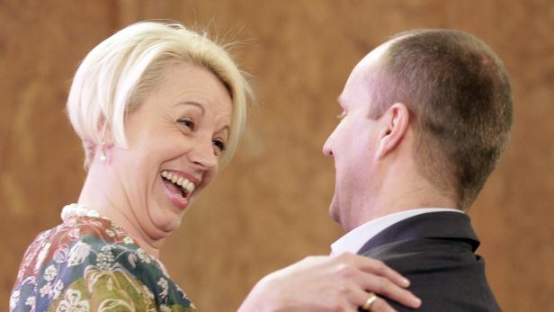 Eine lachende Frau mit blonden Haaren schaut einen Mann im Anzug an.