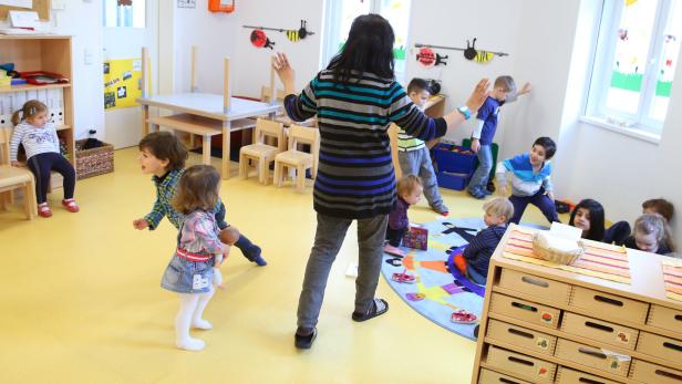 Eine Erzieherin beaufsichtigt eine Gruppe spielender Kinder in einem hellen Raum.