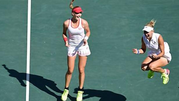 Zwei Tennisspielerinnen springen auf einem Tennisplatz vor Freude in die Luft.