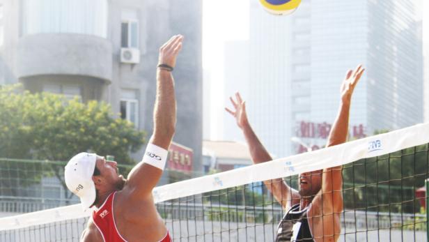 Zwei Beachvolleyballspieler springen am Netz, um einen Ball zu schlagen.