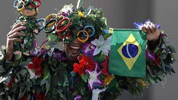 Ein Mann, verkleidet mit Blättern und Blumen, hält eine brasilianische Flagge und eine Puppe mit olympischen Ringen.