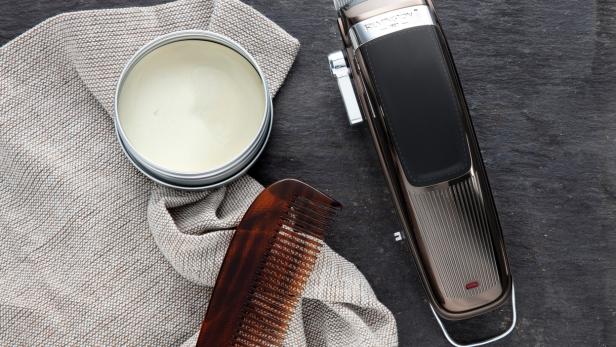 Ein Haarschneider, ein Kamm und eine Dose Haarwachs liegen auf einem Tuch.