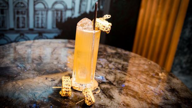 Ein Cocktail in einem hohen Glas, garniert mit gegrilltem Mais.