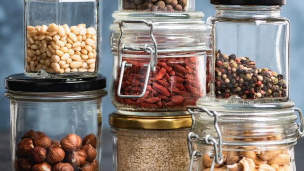 Mehrere Glasbehälter sind mit Nüssen, Samen und Gewürzen gefüllt.