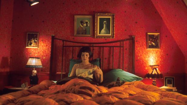 Amélie liest in ihrem rot dekorierten Schlafzimmer ein Buch.